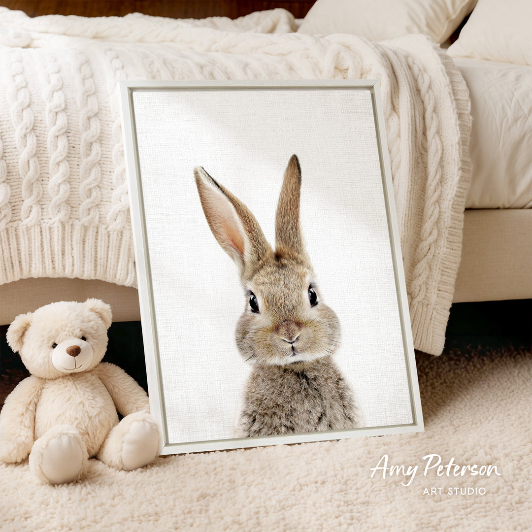 A framed image of a rabbit is displayed on a bed, accompanied by a teddy bear.