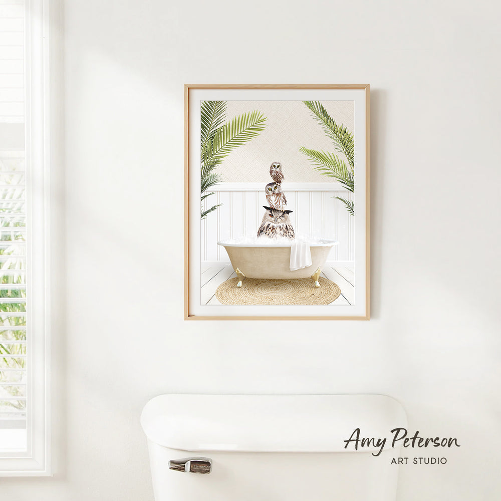 A framed print of a woman sitting in a bathtub, surrounded by tropical plants, hangs on a white wall above a white toilet.