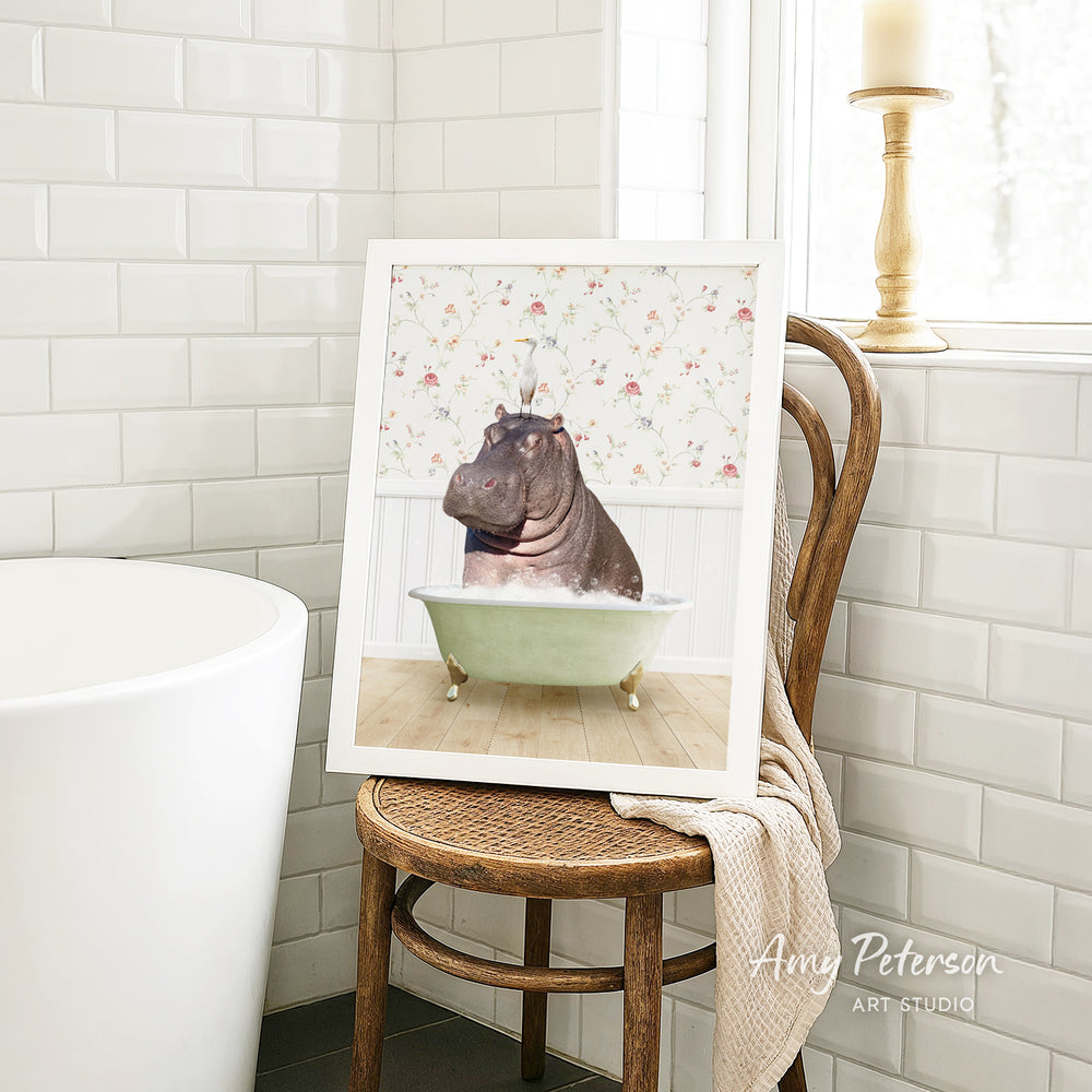 A framed image of a hippopotamus sitting in a bathtub is displayed on a wooden chair in a bathroom setting.