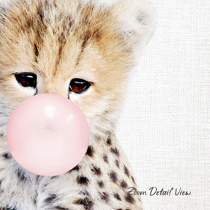 A close-up of a cheetah cub blowing a bubble with a pink bubble gum bubble.
