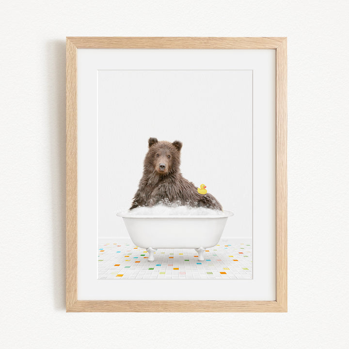 A brown bear sitting in a white bathtub filled with bubbles, with a yellow rubber duck floating nearby.