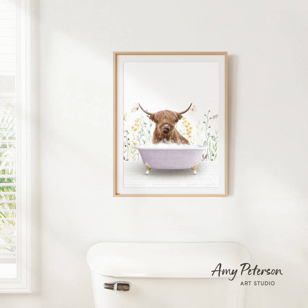 A framed illustration of a Highland cow sitting in a bathtub, surrounded by flowers and plants, is hanging on a white wall.