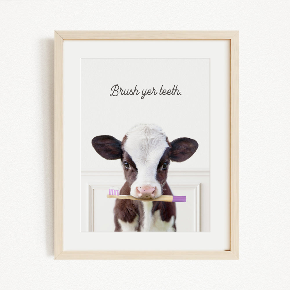 A framed image of a cow holding a toothbrush in its mouth, with the text "Brush yer teeth."