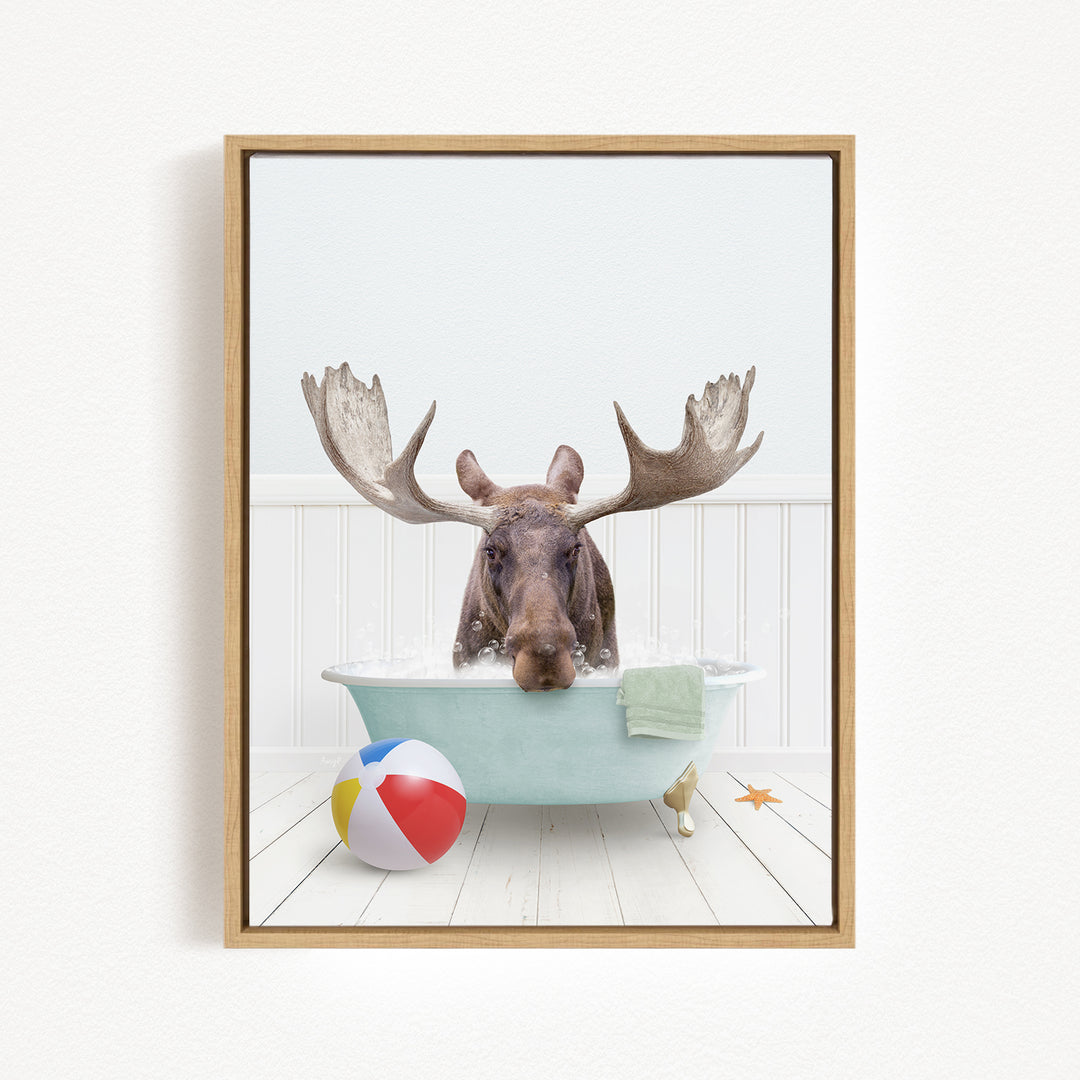 A moose with large antlers is sitting in a bathtub filled with water, surrounded by a beach ball and a starfish.