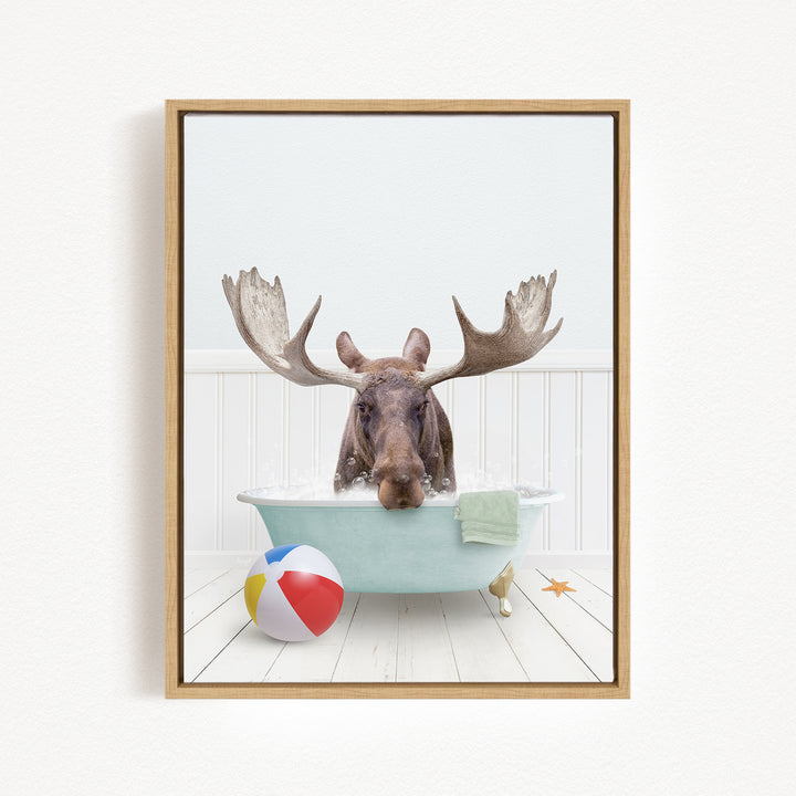 A moose with large antlers is sitting in a bathtub filled with water, surrounded by a beach ball and a starfish.
