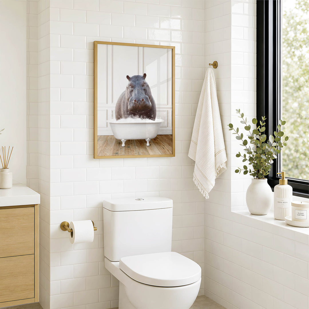 A bathroom with a white toilet, a framed image of a hippopotamus in a bathtub, and a window with greenery on the sill.