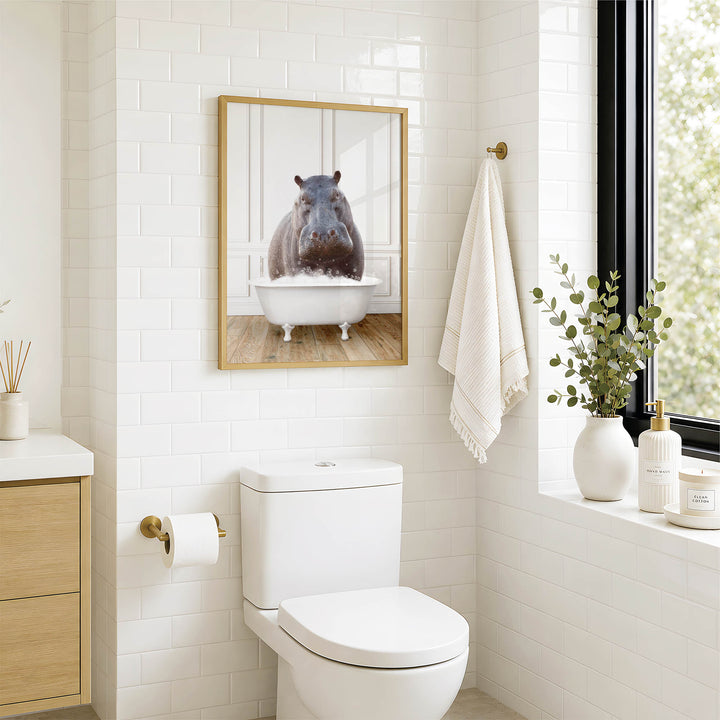 A bathroom with a white toilet, a framed image of a hippopotamus in a bathtub, and a window with greenery on the sill.