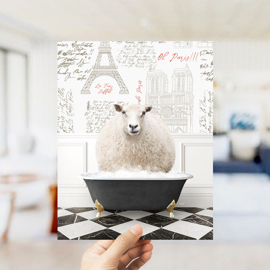 A hand is holding up a framed image of a sheep sitting in a bathtub, with a Paris-themed background featuring the Eiffel Tower and other Parisian landmarks.