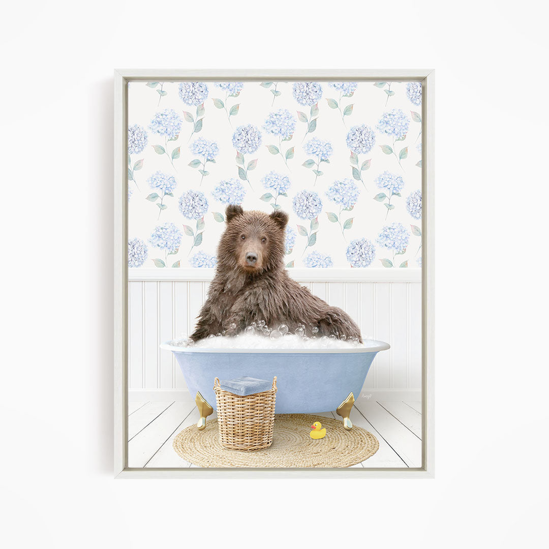 A brown bear sitting in a blue bathtub filled with bubbles, surrounded by a wicker basket and a yellow rubber duck.