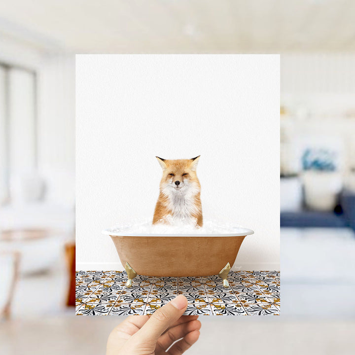 A hand holds up a framed image of a fox sitting in a bathtub filled with bubbles, with a blurred background suggesting a bathroom setting.