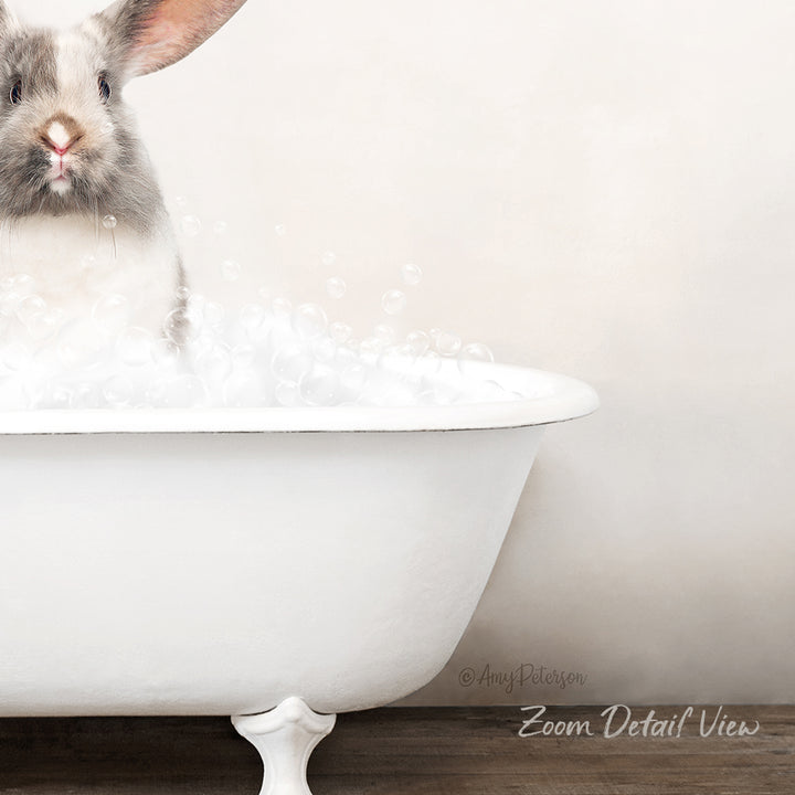A fluffy white rabbit sitting in a white bathtub filled with bubbles, looking directly at the camera.