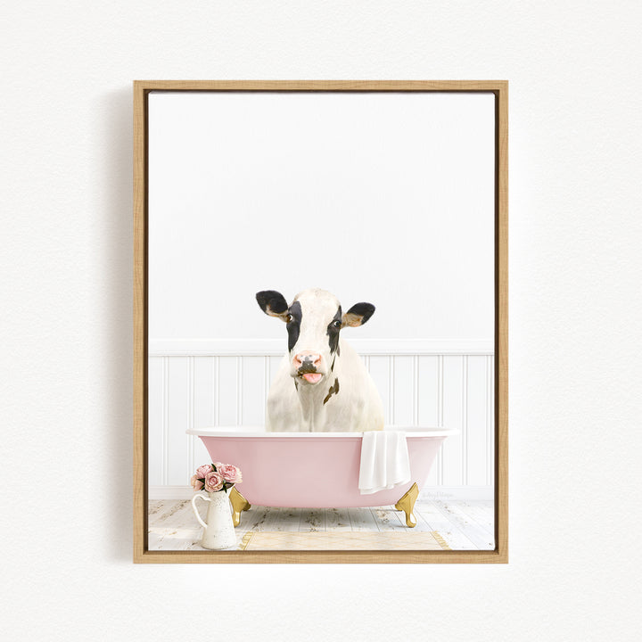 A black and white cow is sitting in a pink bathtub, surrounded by pink flowers and a white vase.