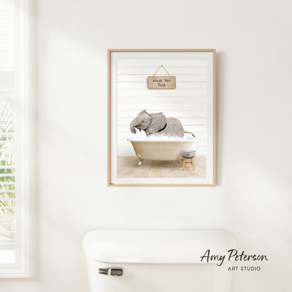 A framed print of an elephant sitting in a bathtub, with a sign above it that says "Wash Your Elephant".