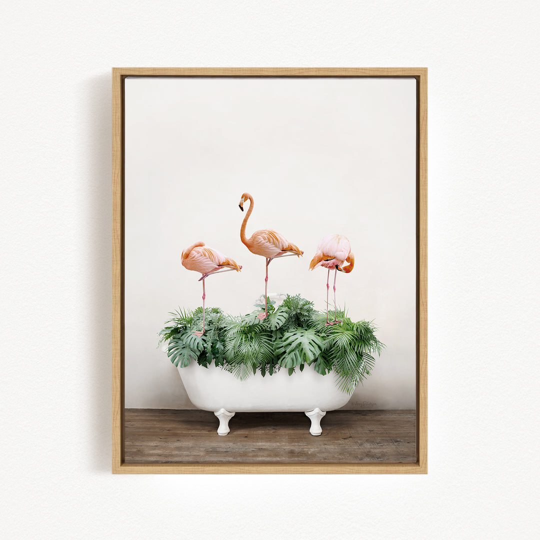A framed image depicting three pink flamingos standing on a white bathtub filled with green plants.