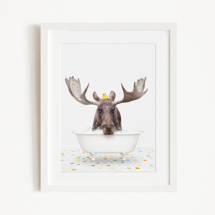 A moose with large antlers is sitting in a white bathtub, with a yellow rubber duck perched on its head.