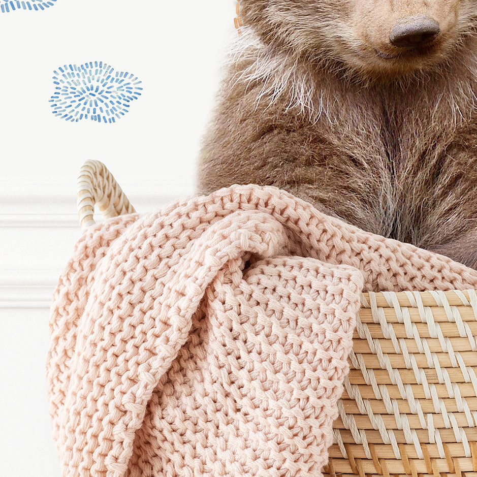 a brown bear sitting on top of a basket next to a blanket