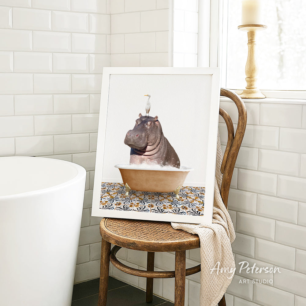 A framed image of a hippopotamus sitting in a bathtub, with a bird perched on its head, is displayed on a wooden chair in a bathroom setting.