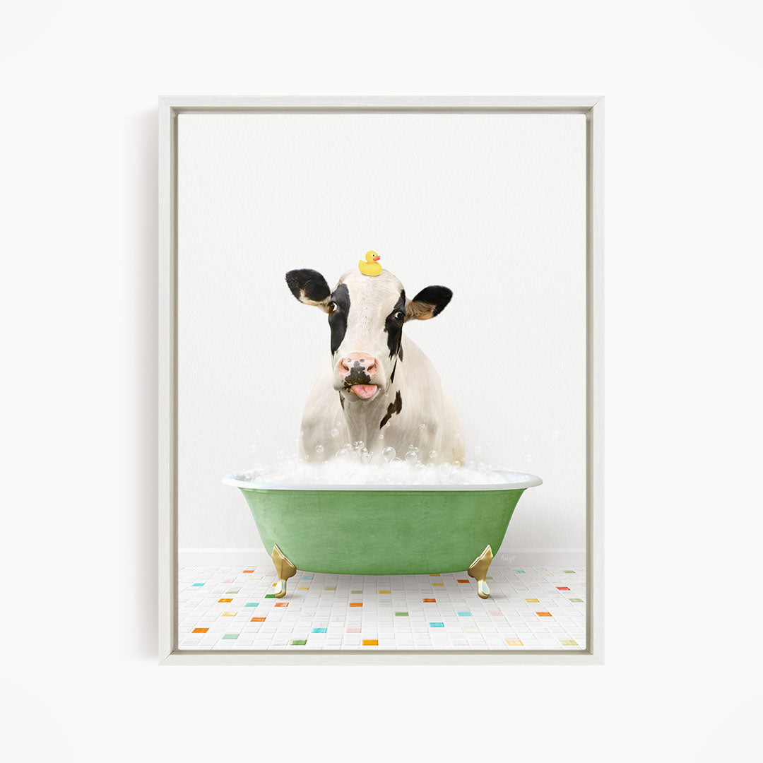 A black and white cow is sitting in a green bathtub filled with bubbles, with a yellow rubber duck perched on its head.