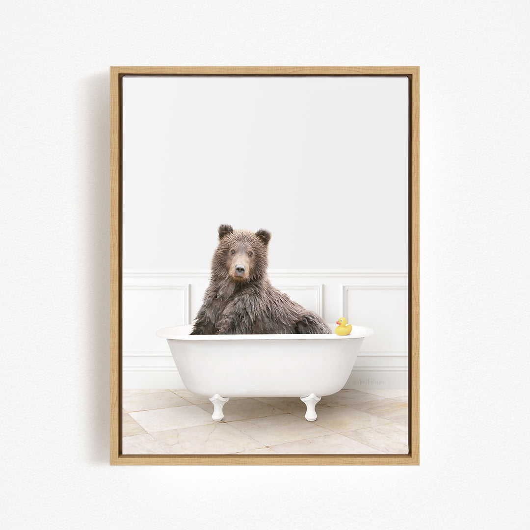 A brown bear sitting in a white bathtub, with a yellow rubber duck floating in the water.