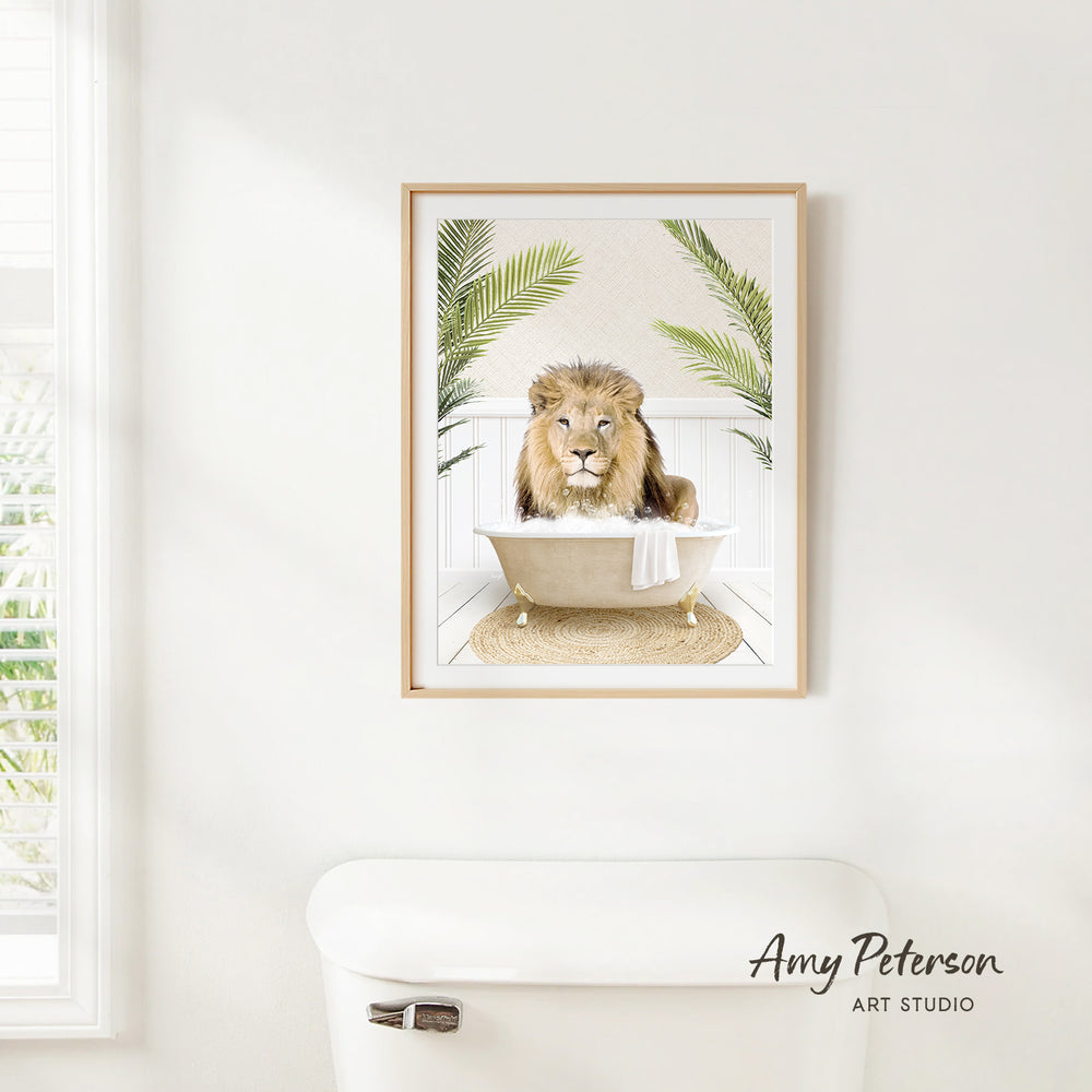 A framed print of a lion sitting in a bathtub, surrounded by palm leaves, is hanging on a white wall in a bathroom.