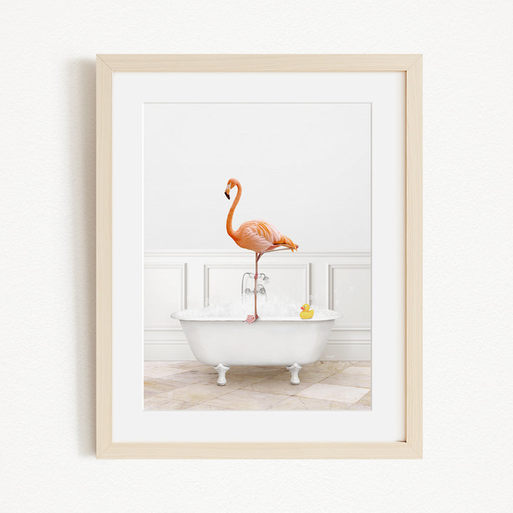 A framed image of a pink flamingo standing on the edge of a white bathtub filled with water and bubbles.