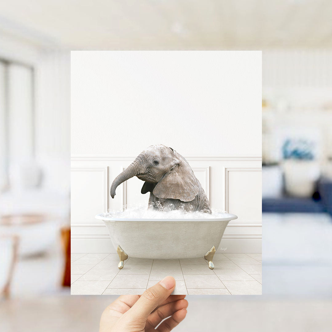 A hand holds up a framed image of a baby elephant sitting in a bathtub filled with water, creating a whimsical and playful scene.