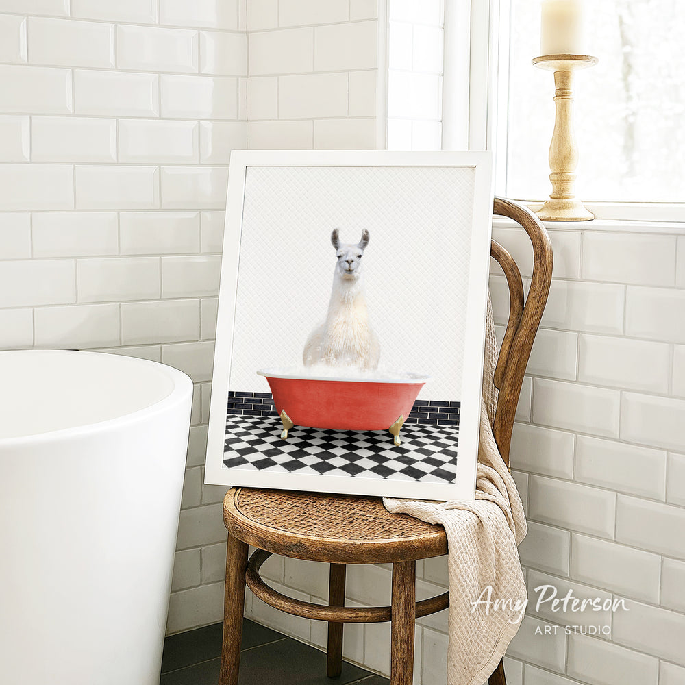 A framed image of a white llama sitting in a red bathtub, placed on a wooden chair in a bathroom setting.
