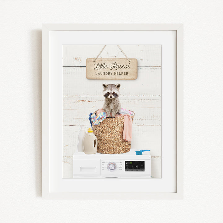 A framed image of a raccoon sitting in a laundry basket, with a sign that says "Little Racquel Laundry Helper" above it.
