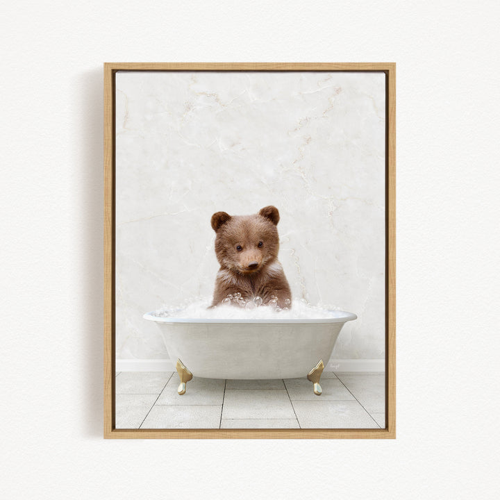 A cute brown bear sitting in a white bathtub filled with bubbles, looking directly at the camera.