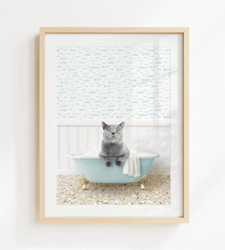 A gray cat sitting in a blue bathtub filled with bubbles, with a patterned shower curtain in the background.