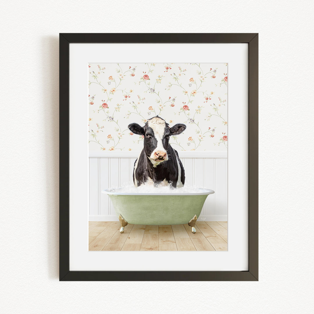A black and white cow is sitting in a green bathtub filled with water, with a floral wallpaper in the background.