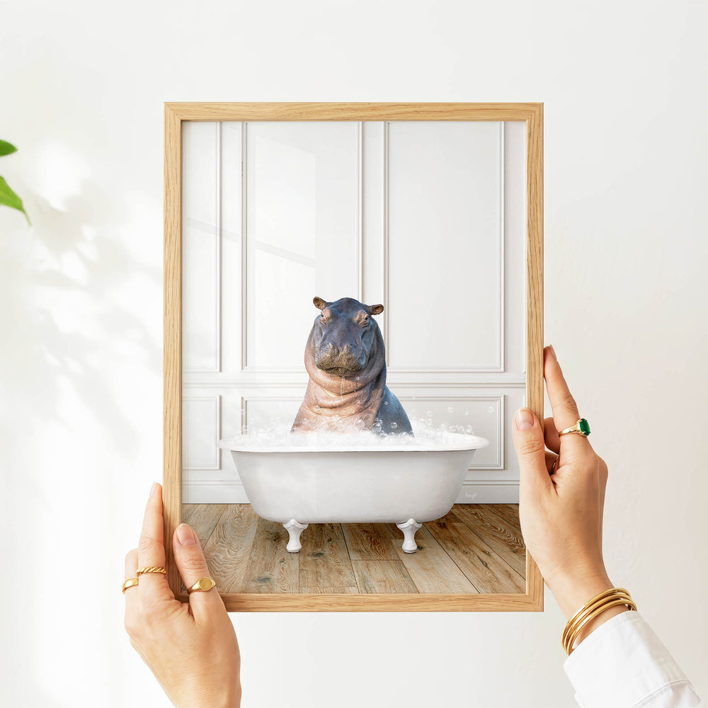 A person's hands are holding a picture frame with a photograph of a hippopotamus sitting in a bathtub.
