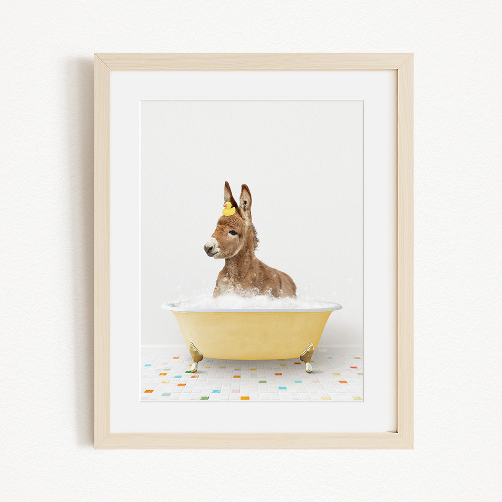 A donkey is sitting in a yellow bathtub filled with bubbles, with a yellow rubber duck floating on the water.