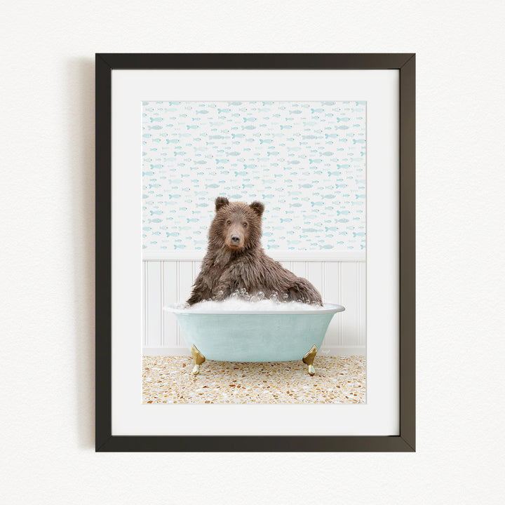 A brown bear sitting in a blue bathtub filled with bubbles, with a patterned wall behind it.