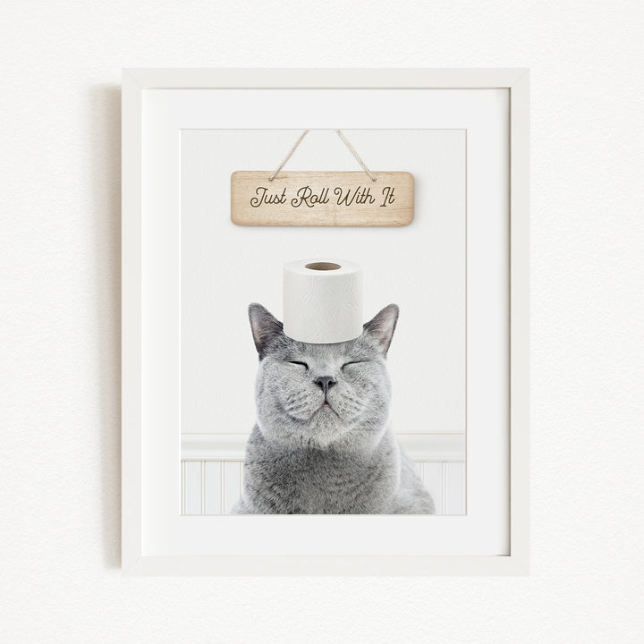 A gray cat with its eyes closed and a roll of toilet paper on its head, with a wooden sign above that says "Just Roll With It".