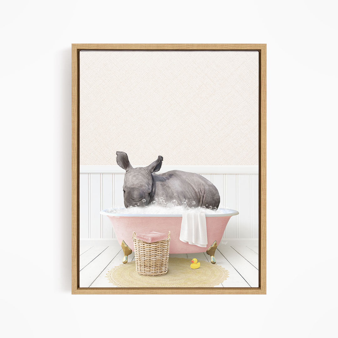 A rhinoceros is sitting in a pink bathtub filled with water, surrounded by a yellow rubber duck and a basket.