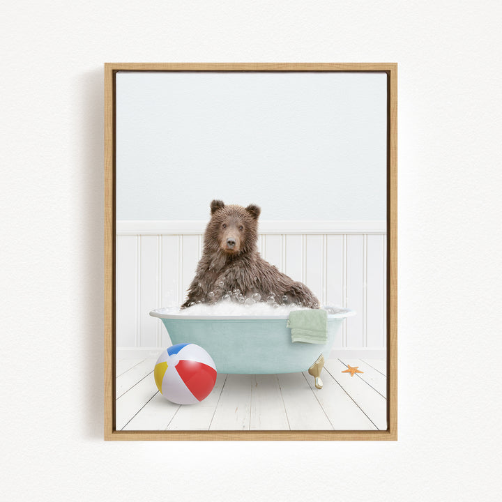 A brown bear sitting in a bathtub filled with bubbles, surrounded by a beach ball and a towel.