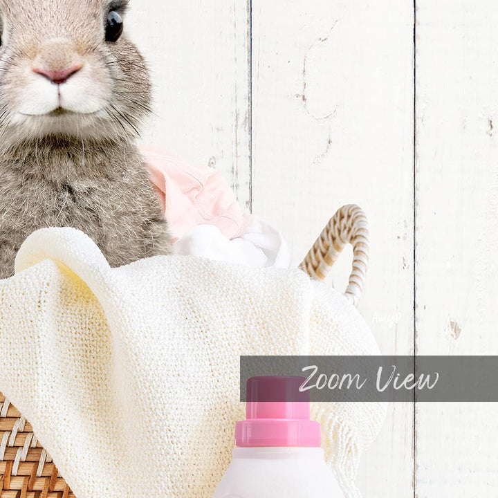 A close-up of a rabbit peeking out from a basket filled with laundry, with a bottle of laundry detergent in the foreground.