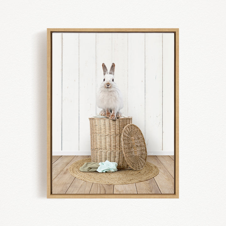A white rabbit sits atop a woven basket on a wooden floor, with a woven basket lid nearby.