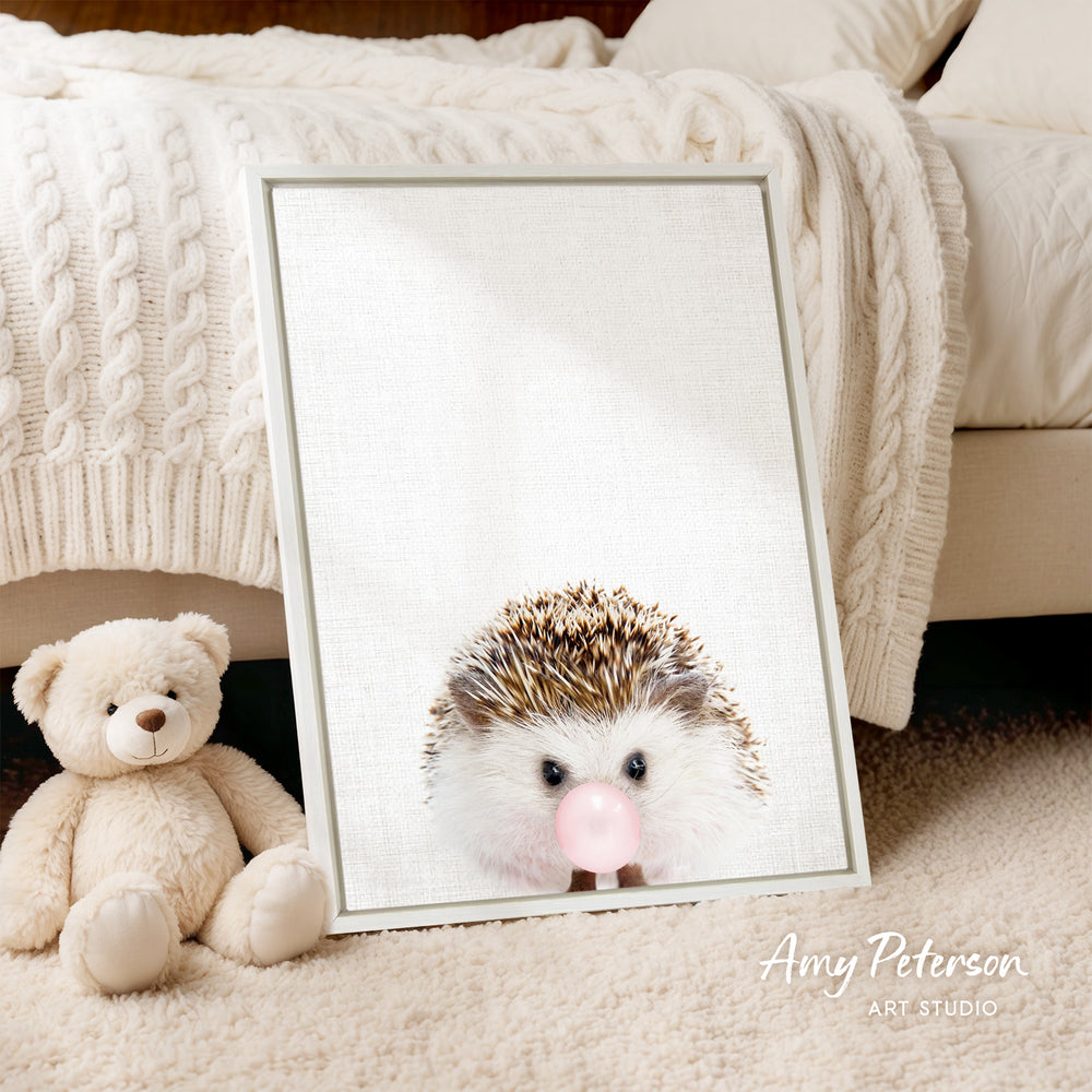 A framed image of a hedgehog blowing a bubble is displayed on a bed, accompanied by a teddy bear.