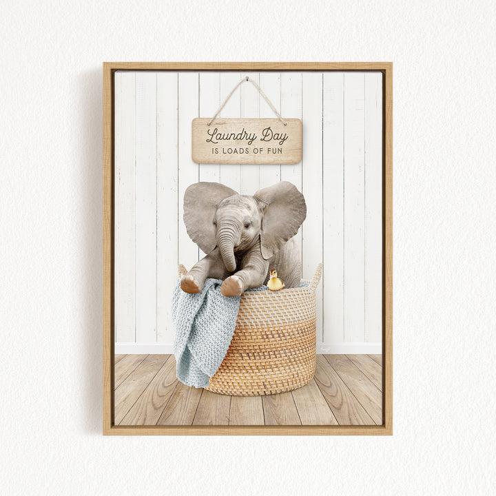 A framed image of a baby elephant sitting in a woven laundry basket, with a sign above that says "Laundry Day is loads of fun".