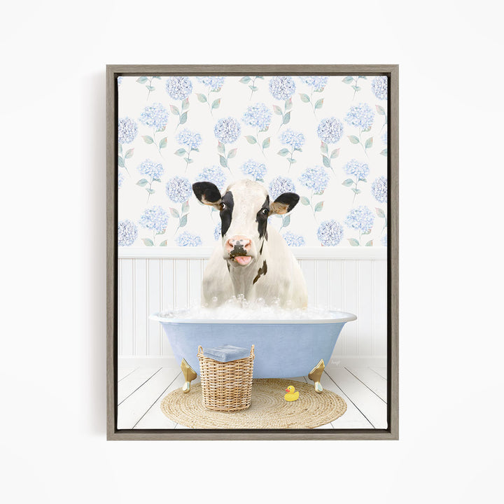 A cow is sitting in a blue bathtub filled with water, surrounded by a wicker basket and rubber ducks.