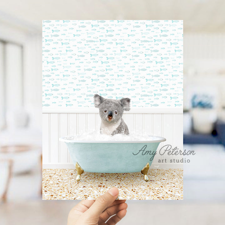 a hand holding a photo of a koala in a bathtub