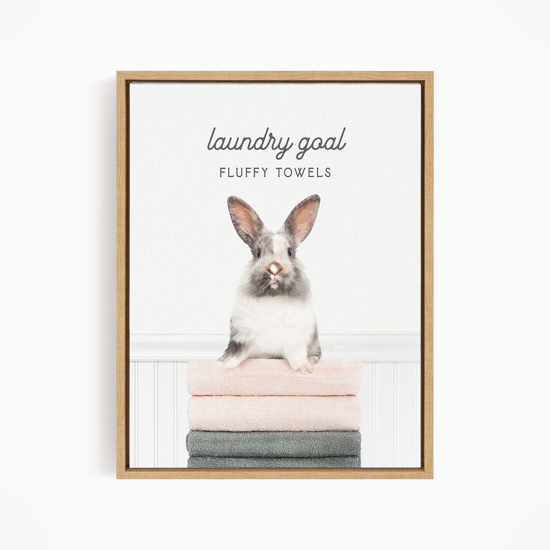 A framed image of a fluffy white rabbit sitting on a stack of towels, with the text "laundry goal FLUFFY TOWELS" written above it.