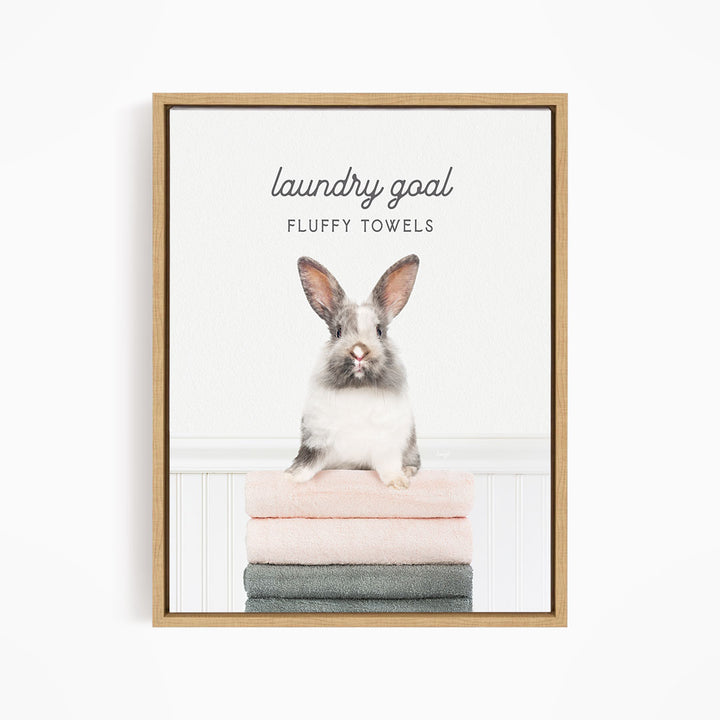 A framed image of a fluffy white rabbit sitting on a stack of towels, with the text "laundry goal FLUFFY TOWELS" written above it.