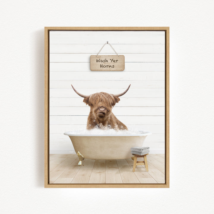 A brown cow with long horns is sitting in a bathtub filled with water, with a sign above it that says "Wash Your Horns".