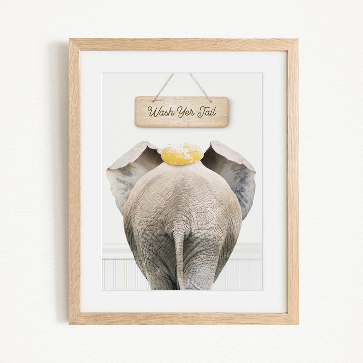 A framed image of an elephant with a sign above it that says "Wash Your Tail".