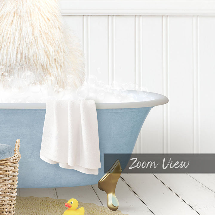 A fluffy white dog is sitting in a blue bathtub filled with bubbles, with a towel and a rubber duck nearby.