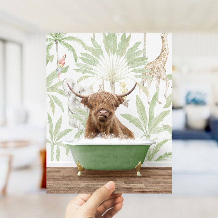 A hand holds up a framed image depicting a brown cow sitting in a green bathtub, surrounded by tropical foliage and animals.