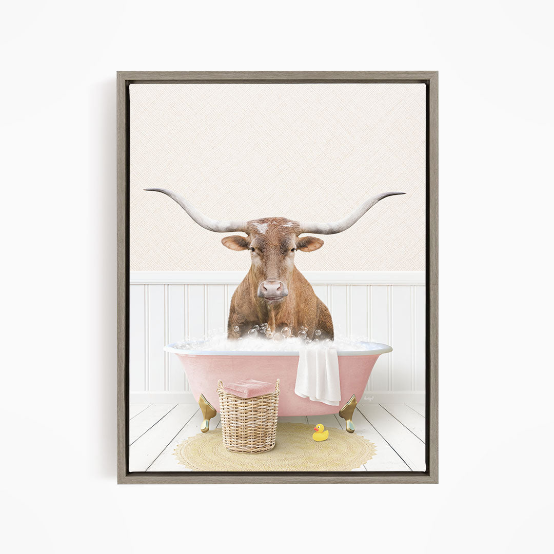 A brown cow with large horns is sitting in a pink bathtub filled with bubbles, surrounded by a yellow rubber duck and a basket.